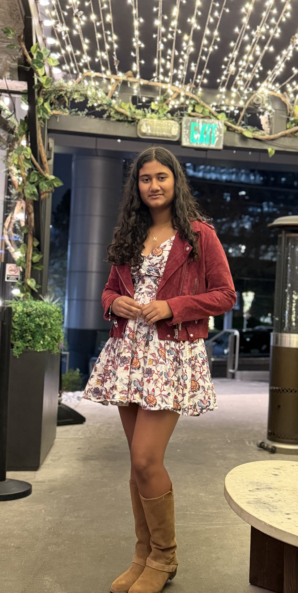 Navya in a floral dress and burgundy jacket under string lights
